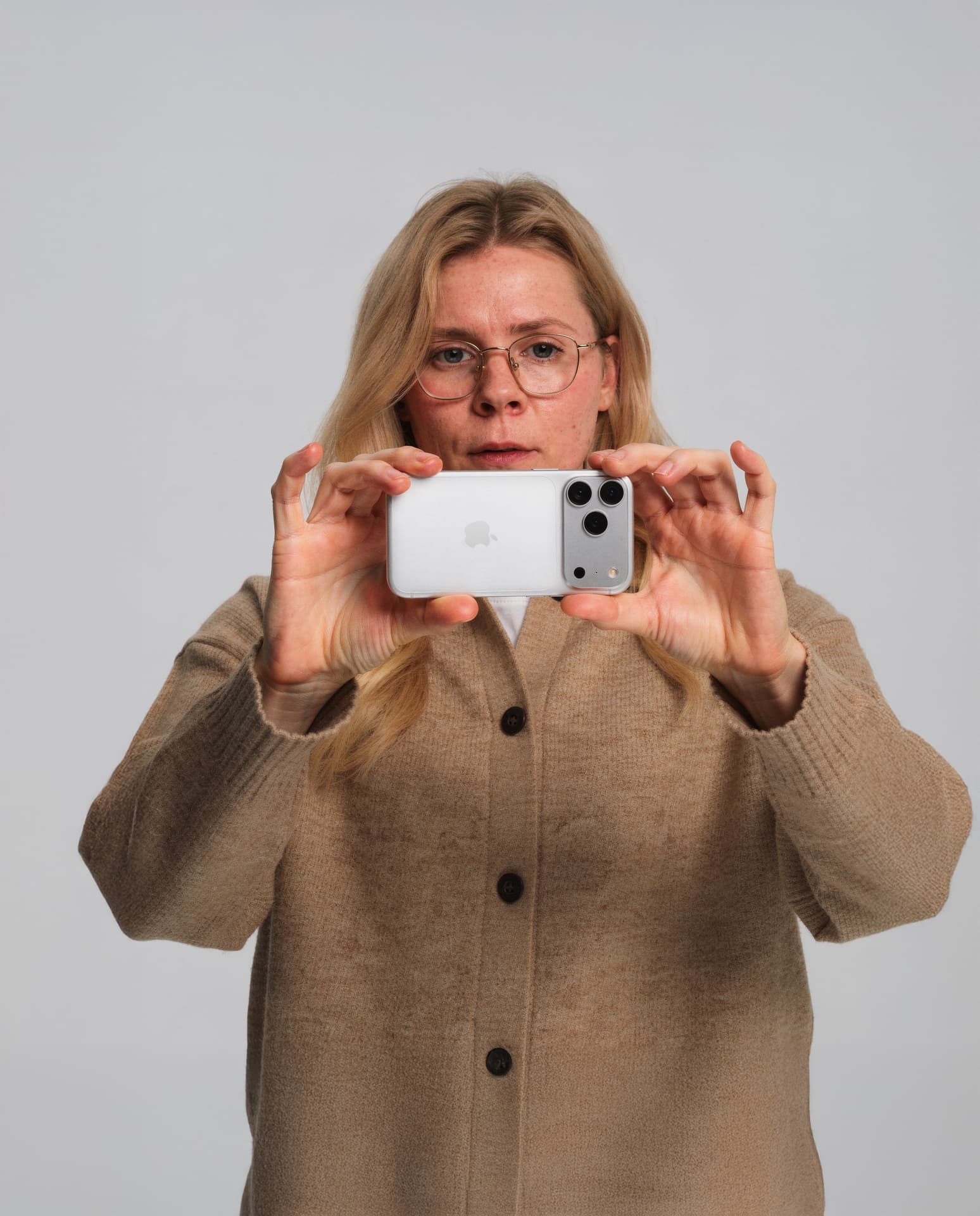 AI-generated character in a beige cardigan and glasses holding a phone horizontally toward the camera