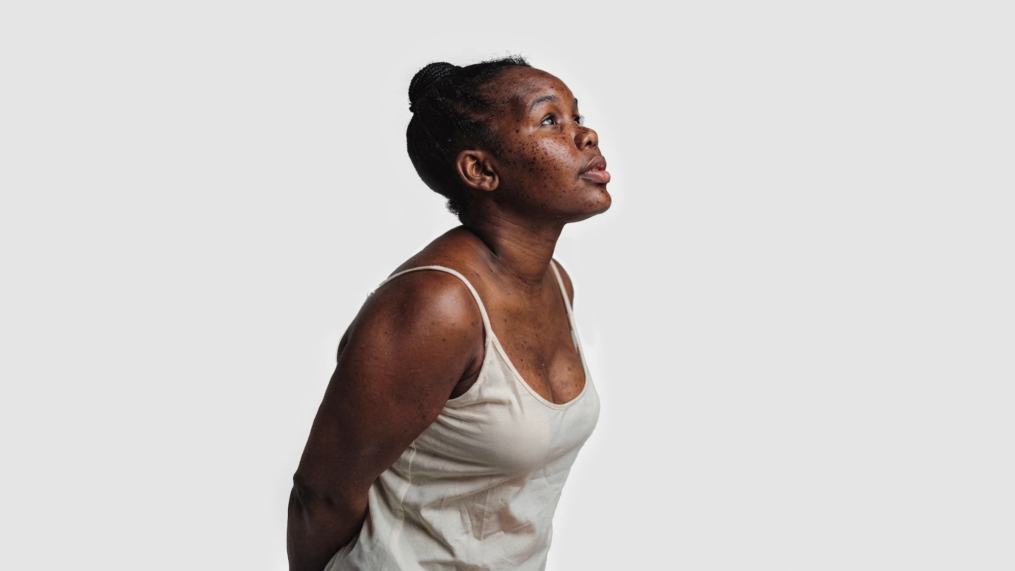 AI-generated side view of the same fictional woman in a cream vest, looking upward, freckled skin