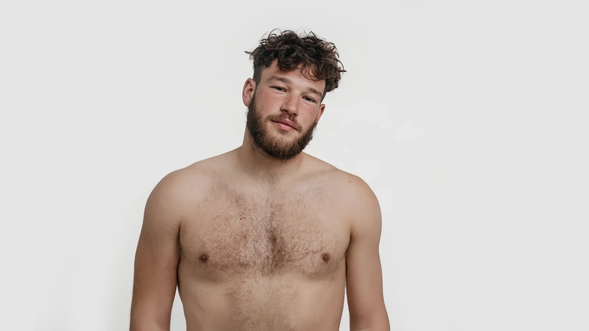 AI-generated front view of a fictional bearded man with curly hair, bare chest and soft build, against a light grey studio background
