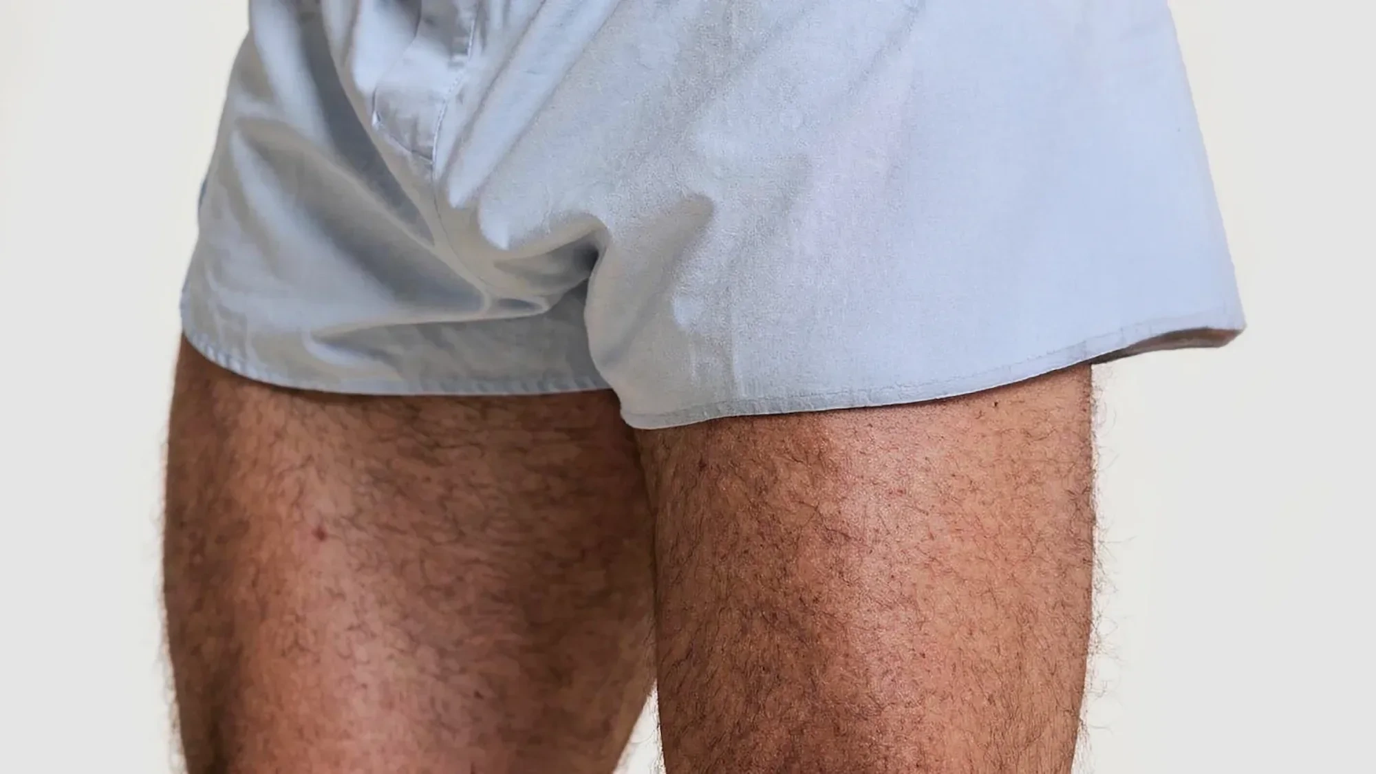 AI-generated close view of two hairy thighs below the hem of pale blue shorts