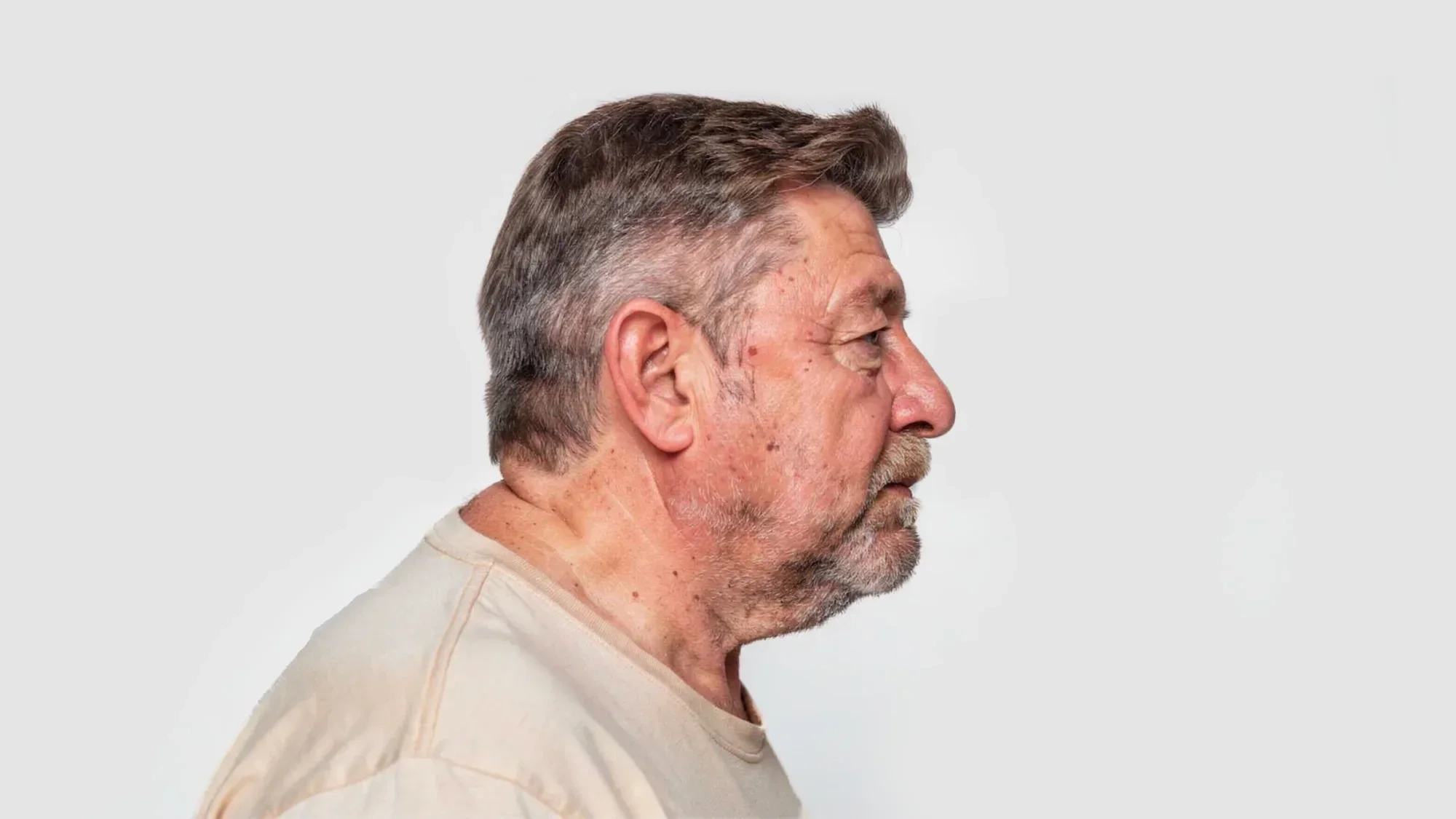 AI-generated side profile of the same fictional older man in a cream t-shirt, looking straight ahead