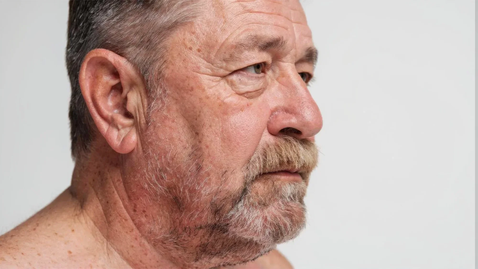 AI-generated close view of the older man's face in profile, showing wrinkles, sun spots and a grey moustache