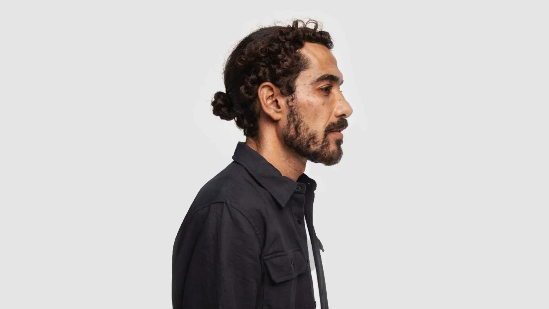 AI-generated side profile of the same fictional man with his hair tied back, in a dark overshirt