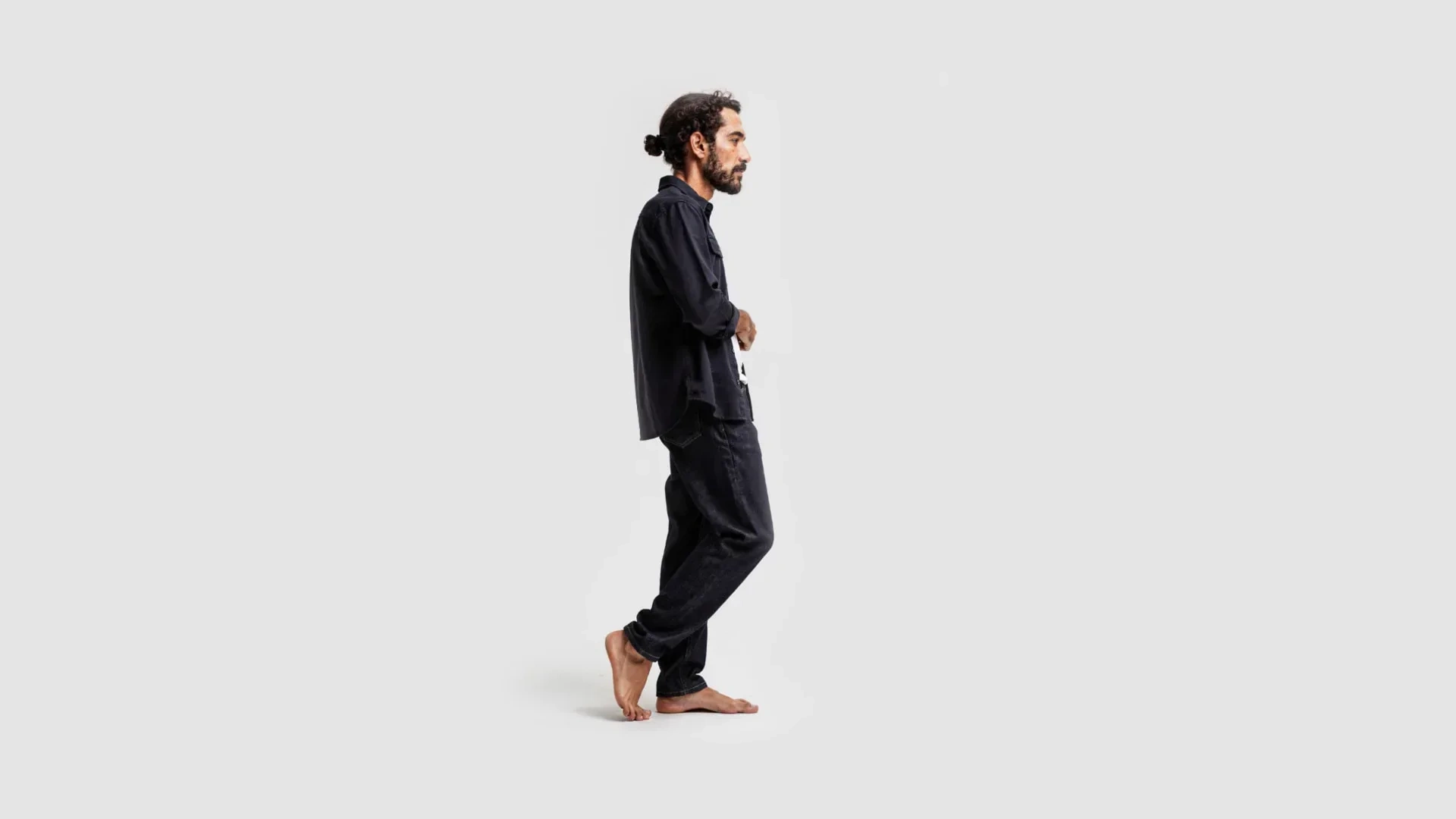 AI-generated full-length side view of the same fictional man barefoot in a dark shirt and jeans, mid-step